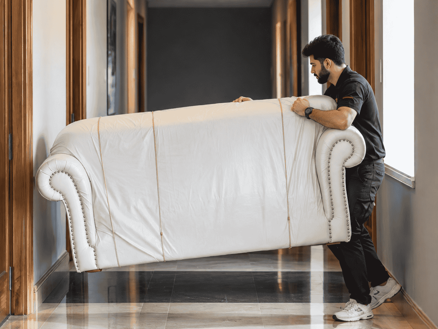 Mover carrying a wrapped sofa through a hallway